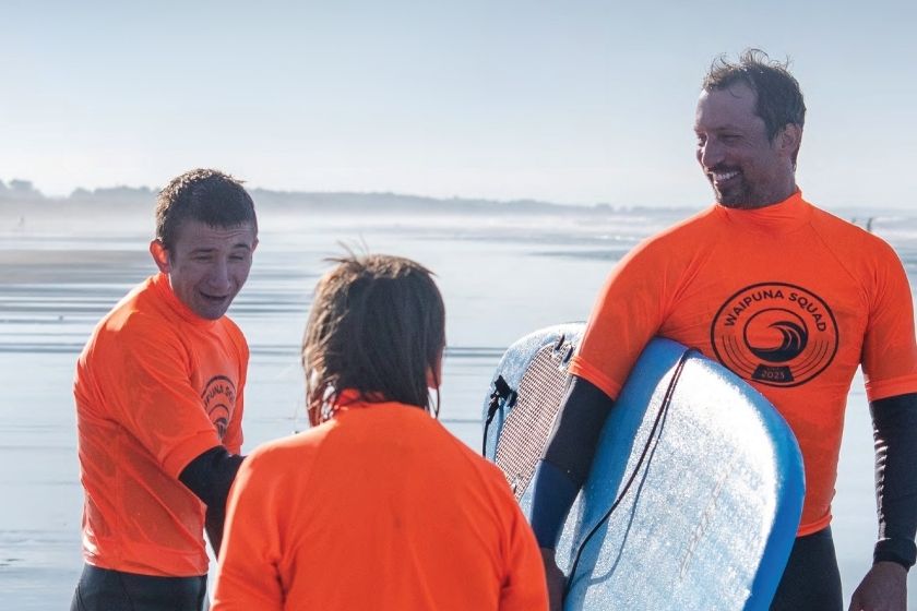 Three people on the beach, one has a surfboard.